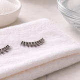 False eyelashes on a clean towel with lash cleansing tools and water bowl.