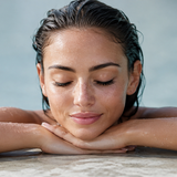 Woman relaxing on the pool edge with wet lash extensions after swimming