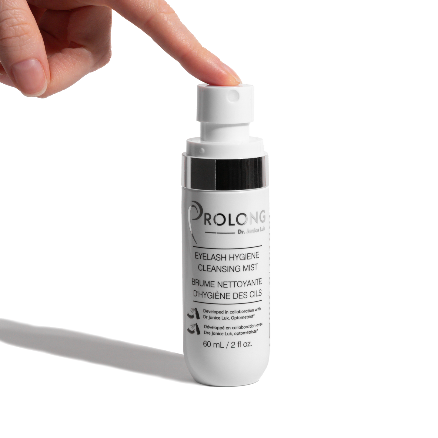 A hand presses the pump of a white bottle labeled Prolong Dr Janice Luk Eyelash Hygiene Cleansing Mist against a clean white background.
